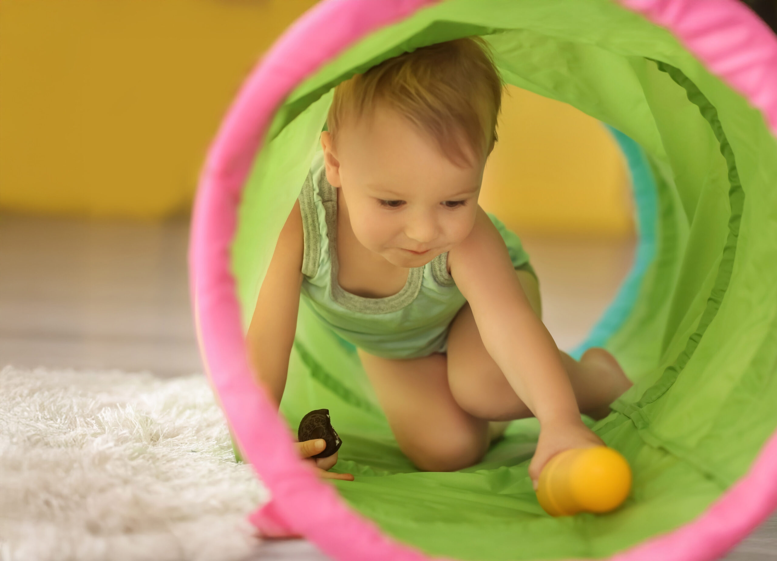 Cute little boy playing with toy tunnel at home