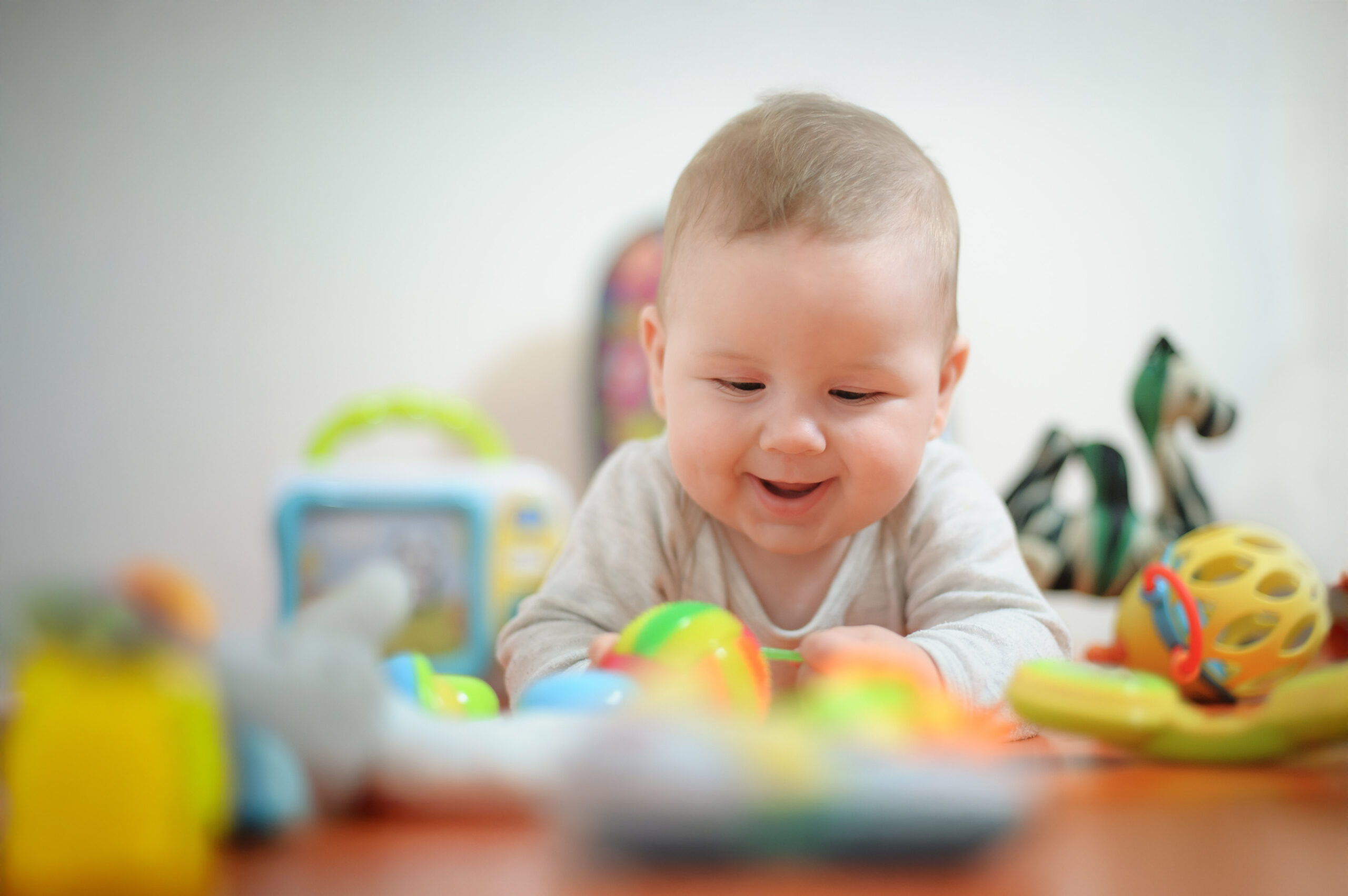 Baby plays with toys. Close-up view of cute baby boy lies on its stomach with an outstretched hand holding a toy and learns about the world around him
