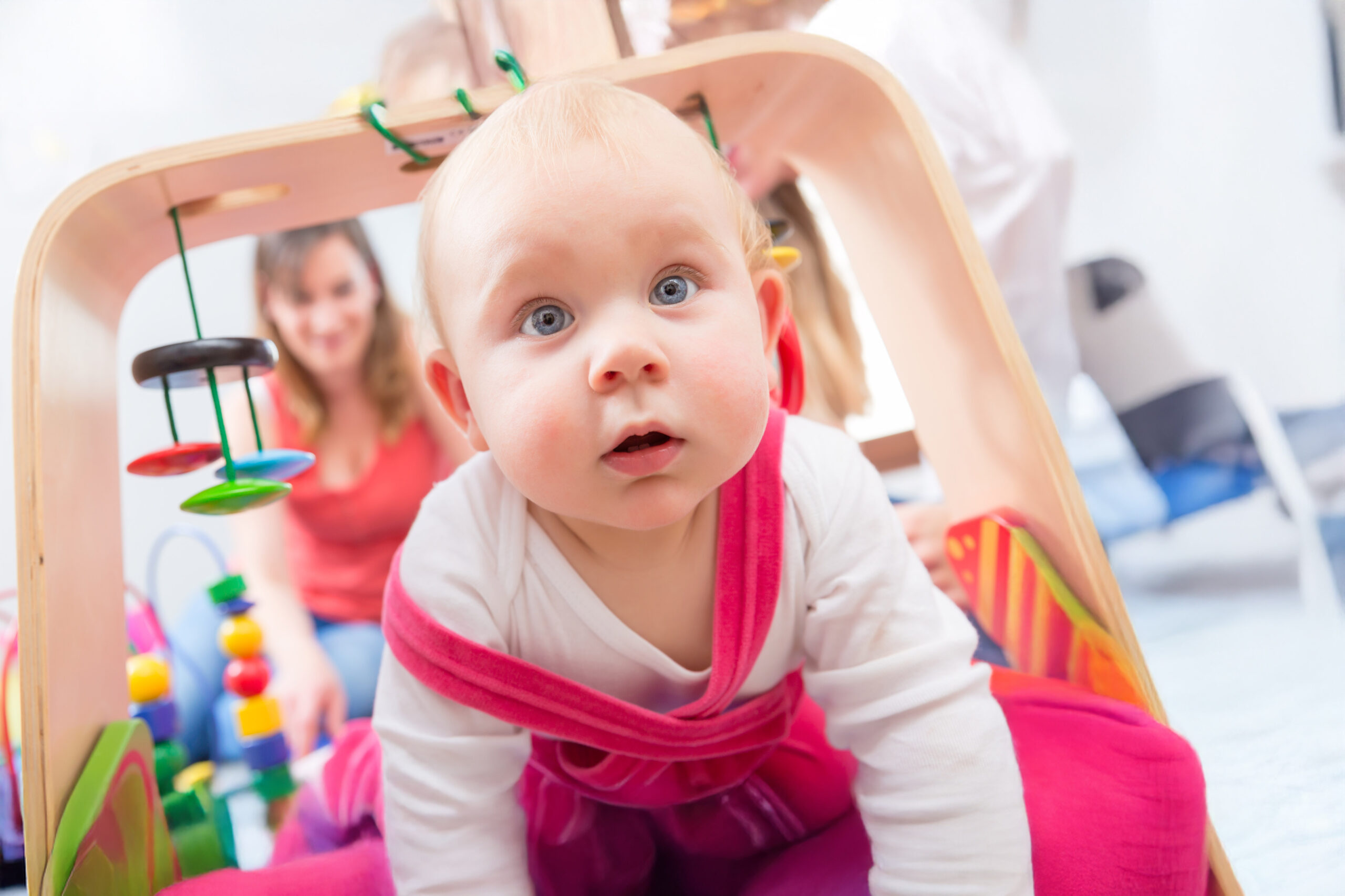 Close-up portrait of a cute baby girl with blue eyes and an intelligent facial expression, while playing on the floor with her mother at home